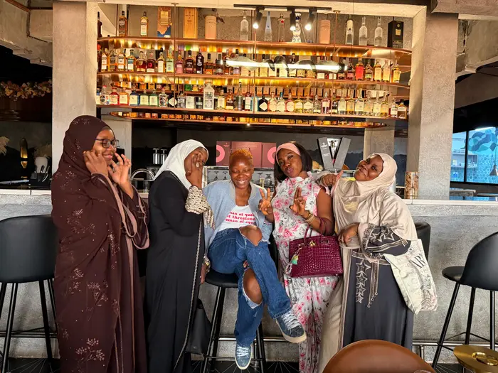 Five women posing playfully together at a restaurant bar