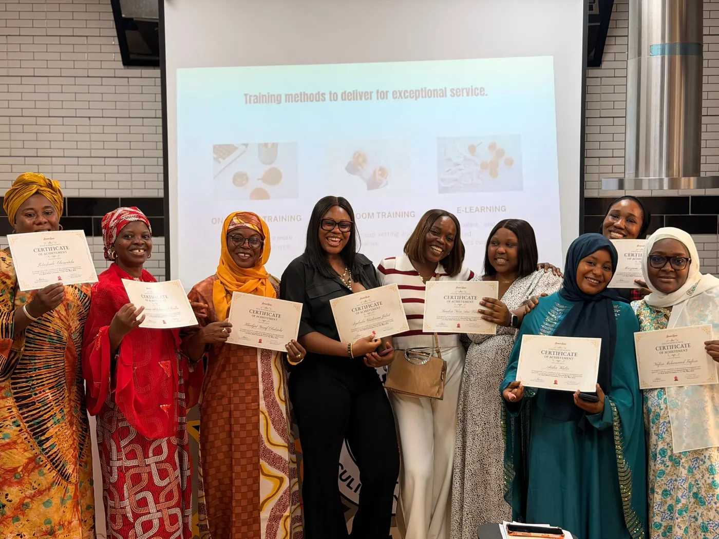 A cohort of graduates holding up their Almond Rouge certificates of achievement