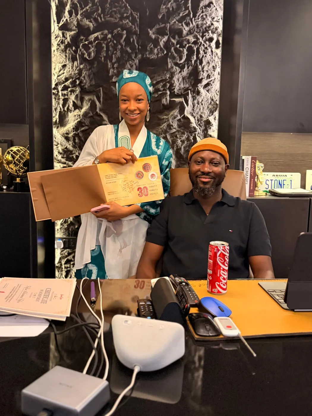 A student holding an open cookbook beside a chef at his desk