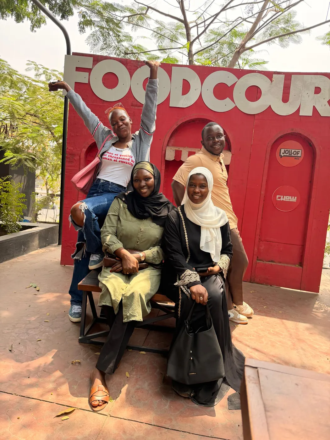 Four people posing in front of a bright red food court wall