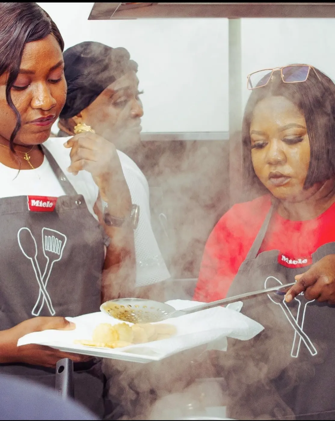 Two cooks lifting freshly fried food from the oil, steam rising